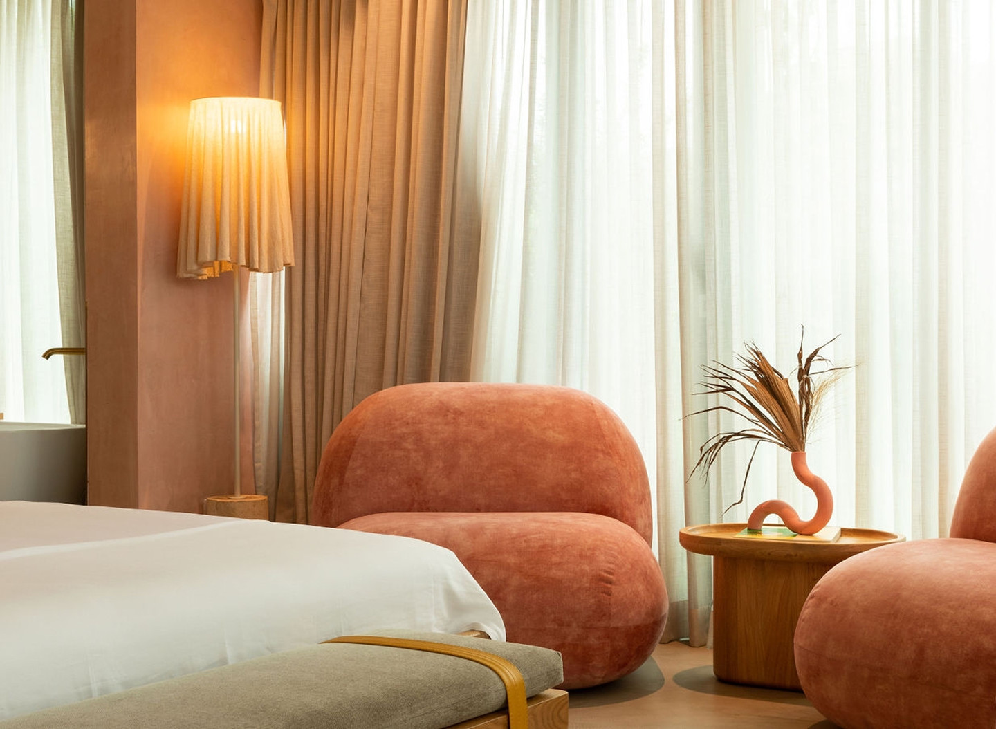 A hotel room featuring a bed and two pink chairs, creating a cozy and inviting atmosphere.