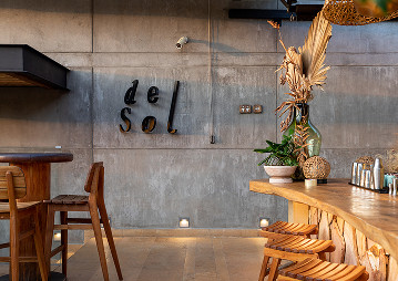 Bar del hotel Del Sol, con mesas y sillas al aire libre, decorado con luces cálidas y plantas tropicales.