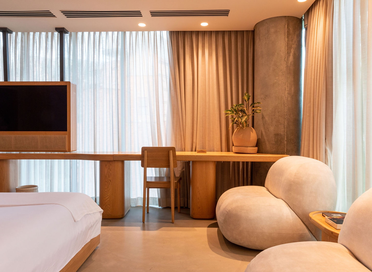 A hotel room featuring a neatly made bed, a comfortable chair, and a flat-screen television on the wall.