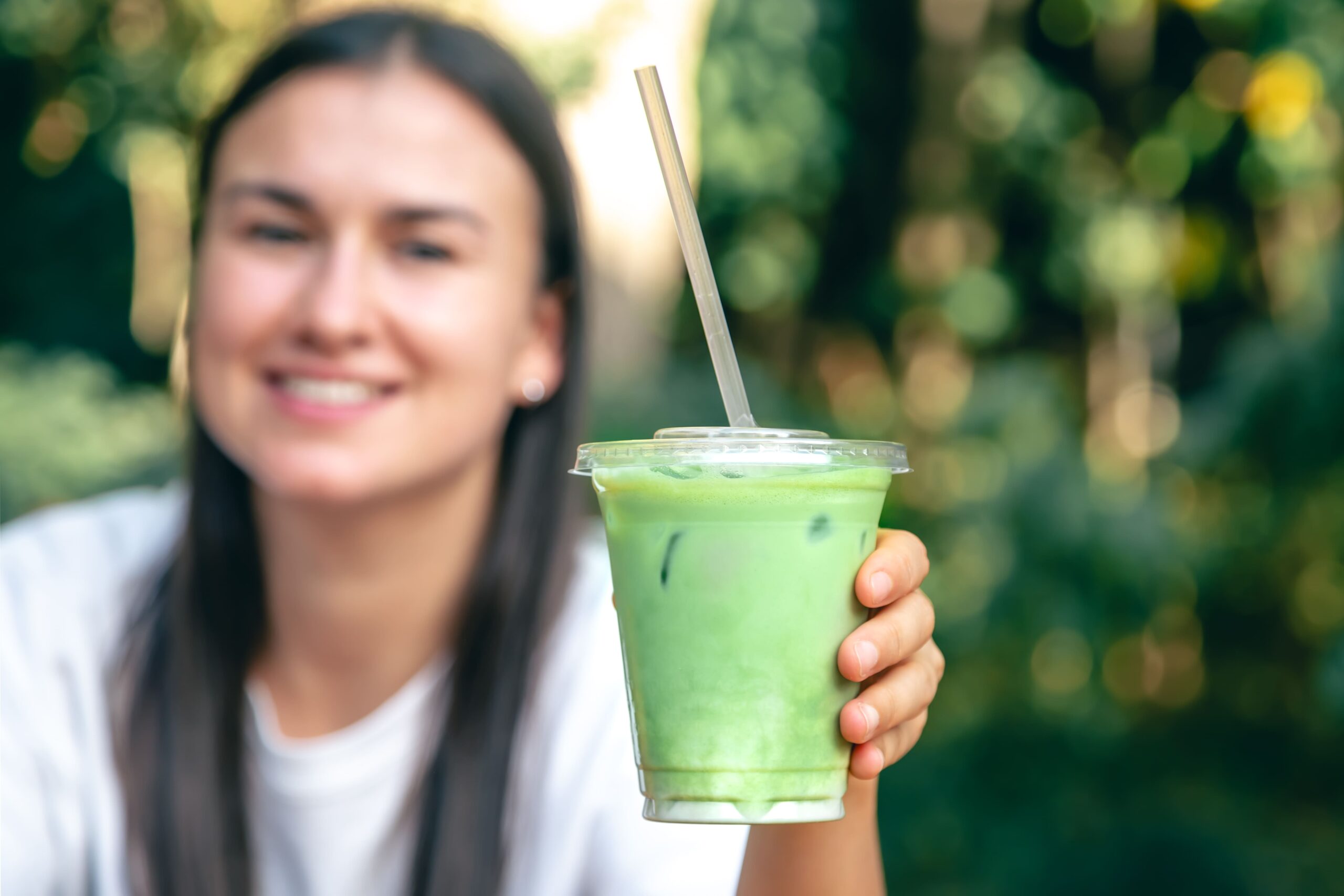Mujer sosteniendo un batido verde con una pajilla, sonriendo y disfrutando de su bebida saludable.