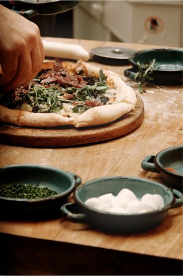 A person carefully placing toppings on a pizza on a table, highlighting the preparation of a homemade dish