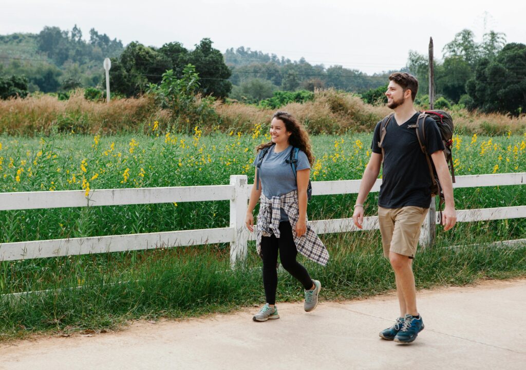Two people walking along a path beside a green field under a clear blue sky.