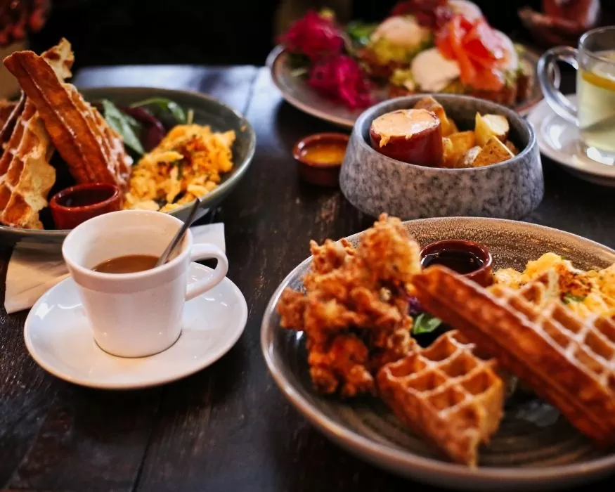 Mesa con waffles, huevos y una taza de café humeante, lista para un desayuno delicioso.