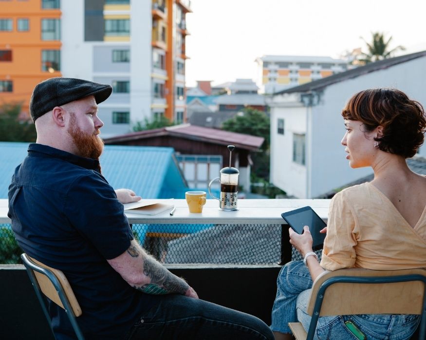 Un hombre y una mujer sentados en un balcón, mirando un tablet juntos en un ambiente relajado.