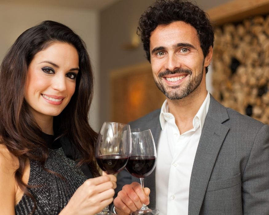 Un hombre y una mujer sosteniendo copas de vino, sonriendo en un ambiente festivo.