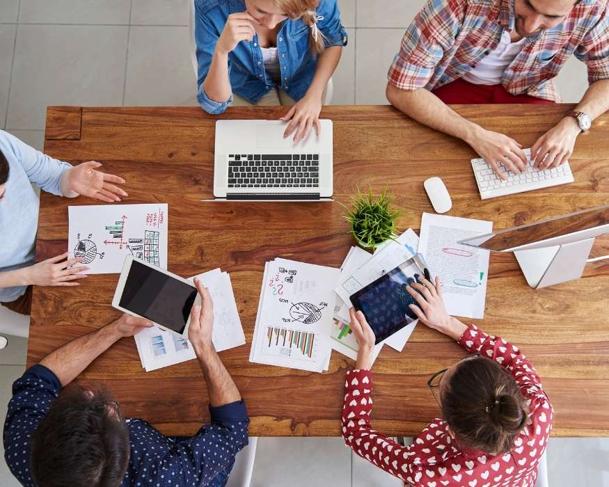 Un grupo de personas sentadas alrededor de una mesa con laptops, colaborando en un ambiente de trabajo.