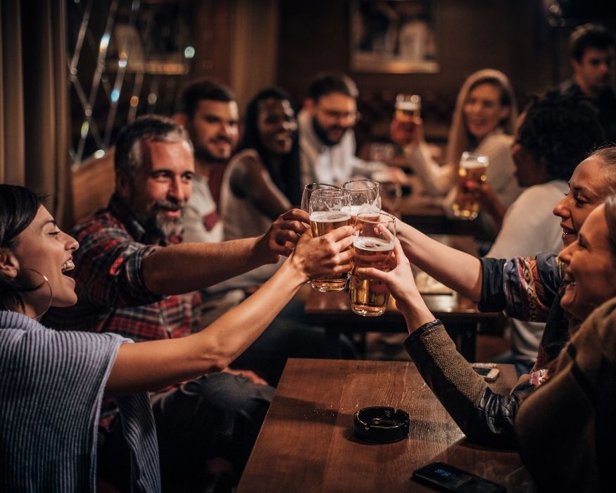Un grupo de personas brindando con cervezas en un pub animado.
