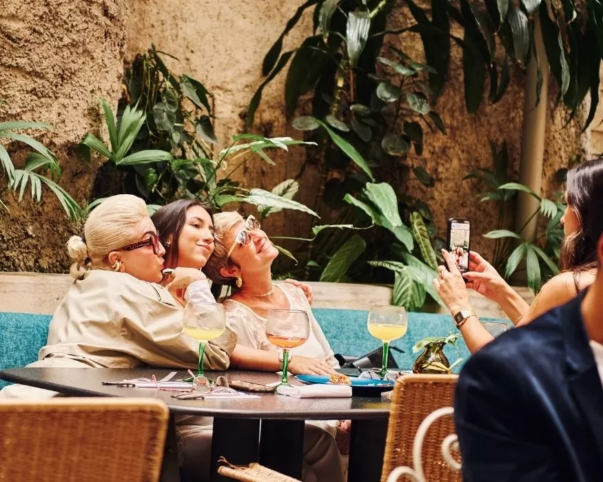 A table with three women sharing food and drinks, engaged in conversation and laughte