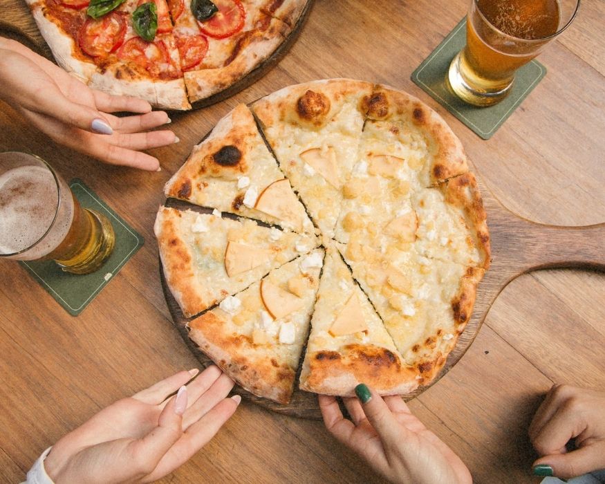 Un grupo de personas sostiene porciones de pizza sobre una mesa de madera