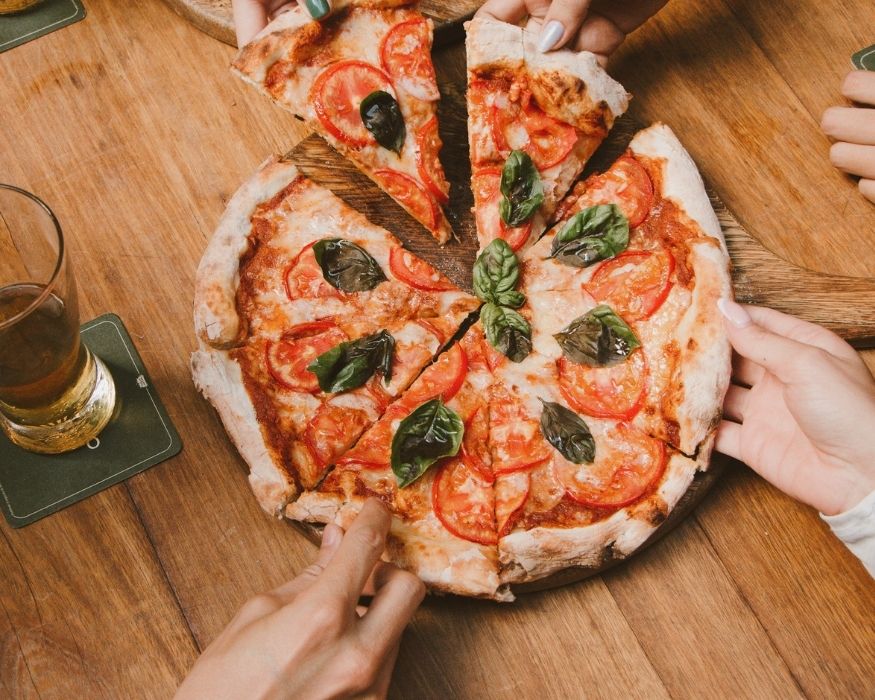 Several individuals proudly display a pizza adorned with ripe tomatoes and basil, emphasizing a shared culinary experience