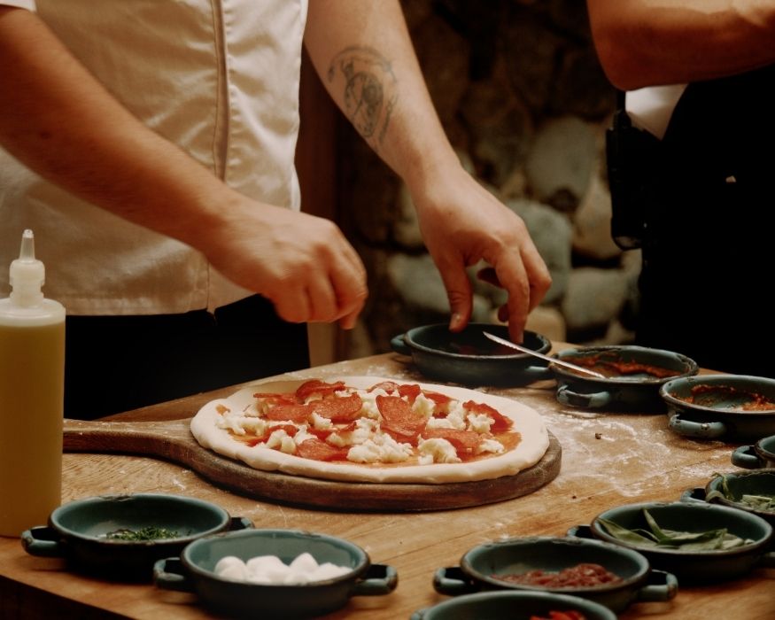 Chef en acción, elaborando una pizza en una mesa de madera, rodeado de ingredientes.