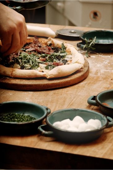 Persona decorando una pizza con diversos toppings en una mesa