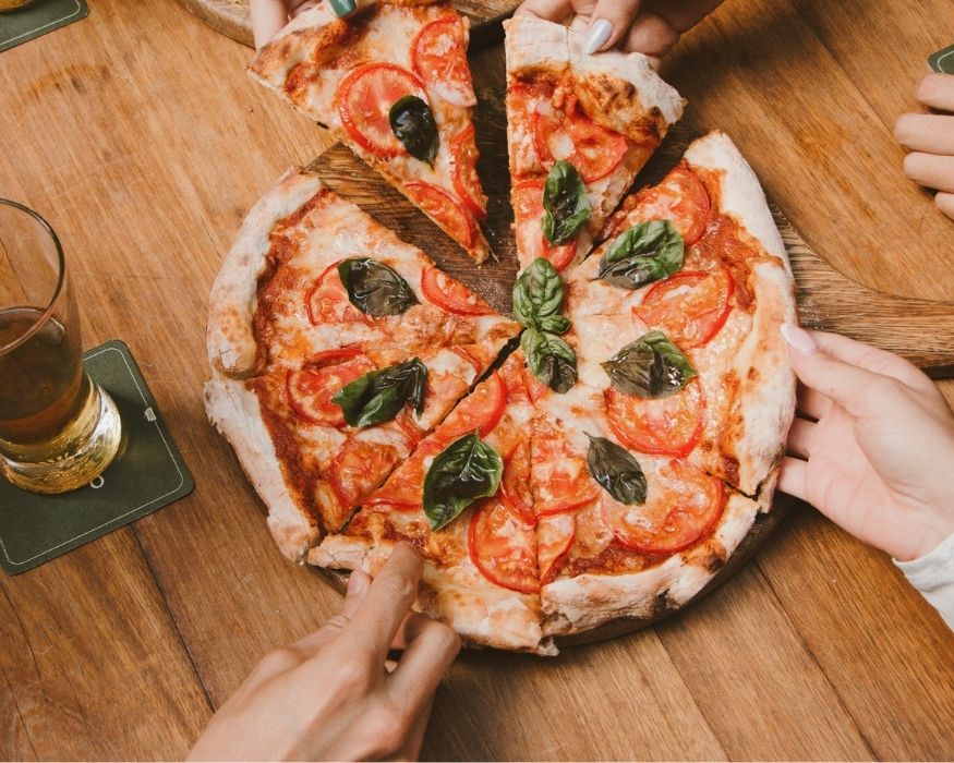 Varias personas muestran una pizza con tomates y albahaca, sonriendo y disfrutando del momento