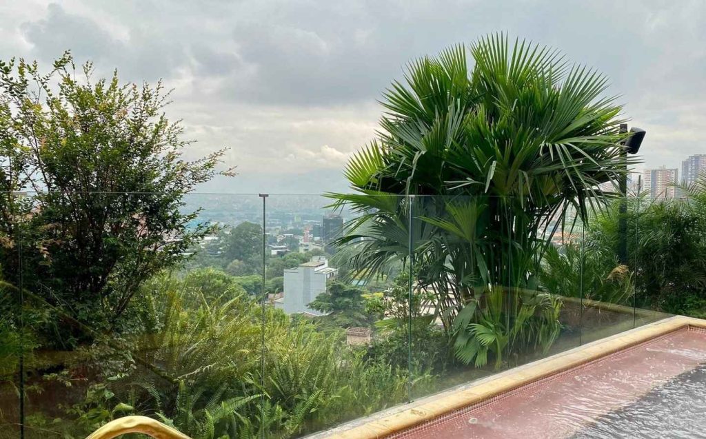 Vista de la ciudad desde un balcón con piscina, mostrando edificios y un cielo despejado.