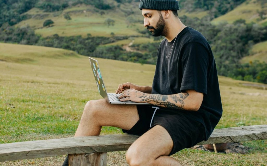 nomada digital con tatuajes en un banco, concentrado en su laptop con wifi