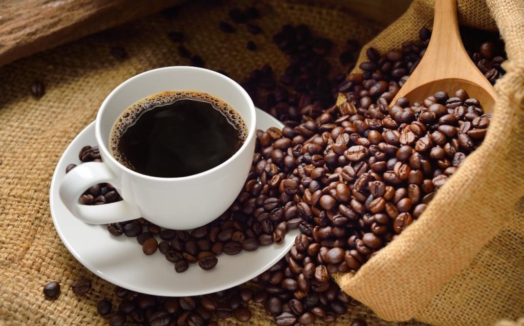 Granos de café y una taza de café sobre un tejido de yute