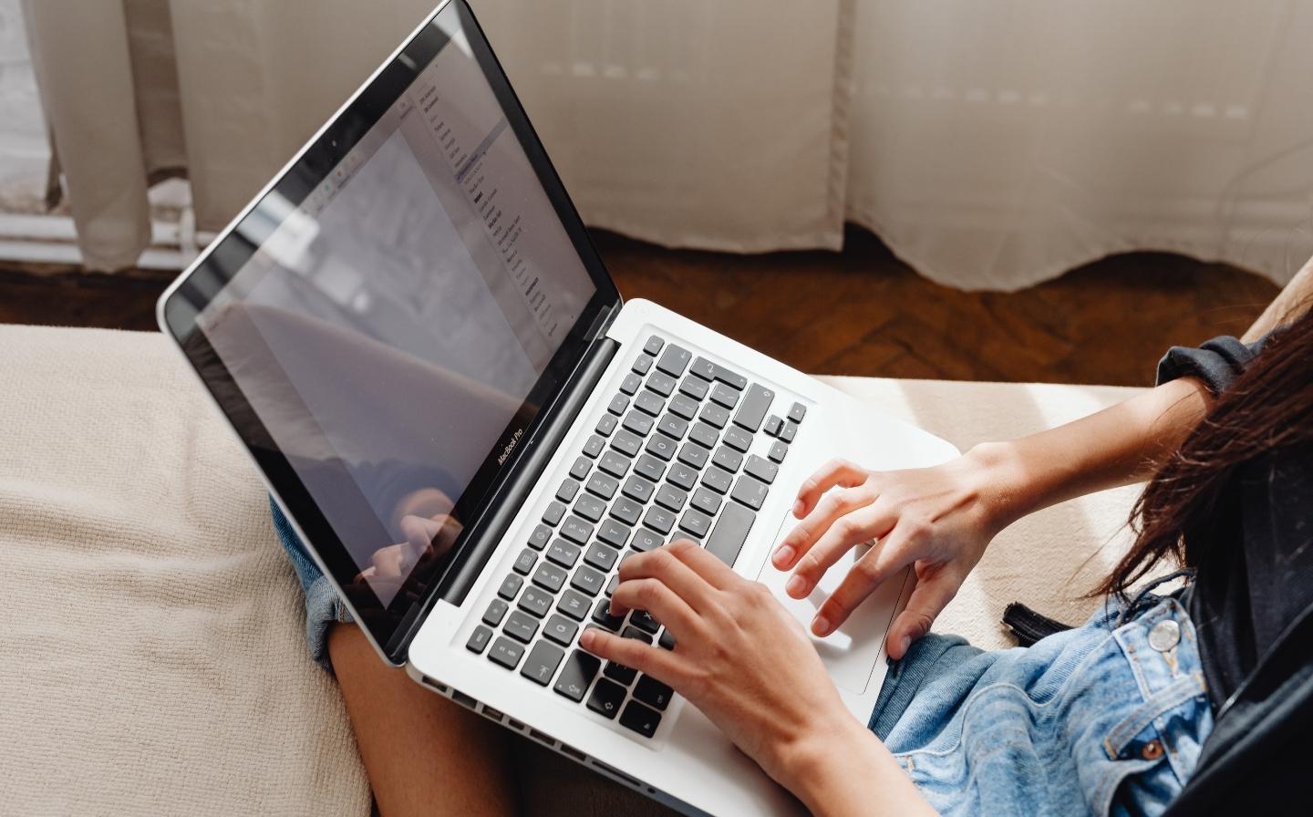 Mujer sentada en un sofá con su laptop, comparando Airbnb y hoteles boutique