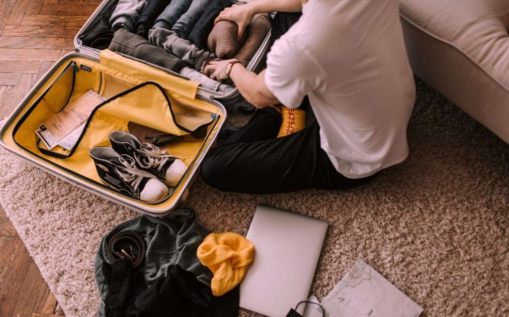 Persona sentada en el suelo con una maleta y una laptop, lista para un viaje ligero de 3 días a Medellín