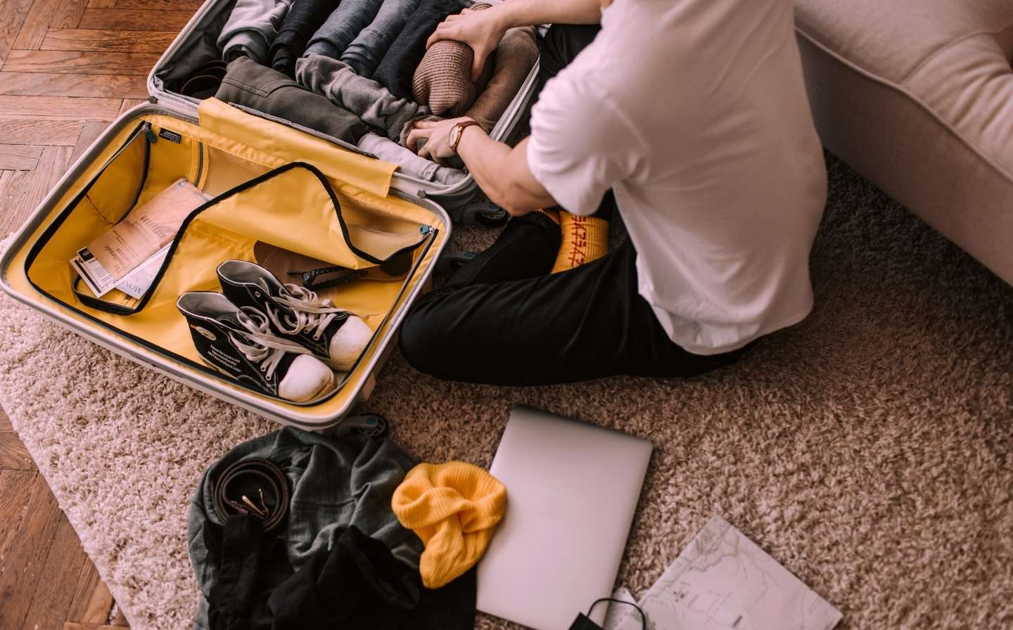 Persona sentada en el suelo con una maleta y una laptop, lista para un viaje ligero de 3 días a Medellín