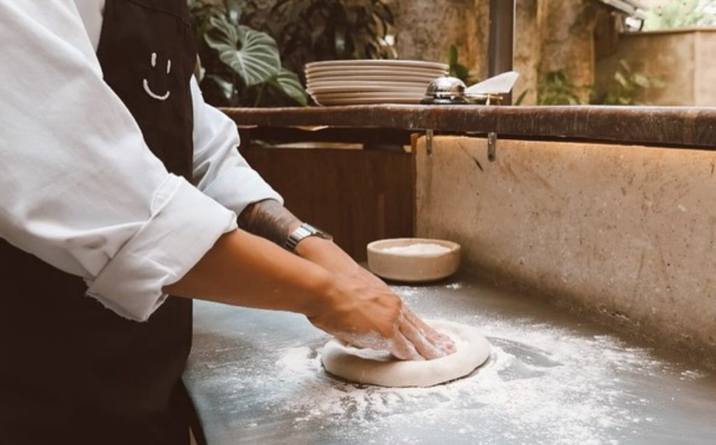 A chef kneads dough on a countertop, preparing for a creamy vegan pizza recipe