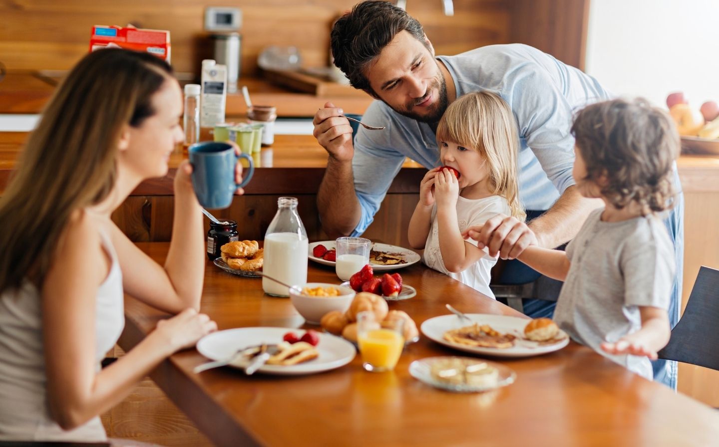 Una familia disfrutando de un desayuno juntos en la mesa de la cocina, sonrisas y platos llenos de comida deliciosa.
