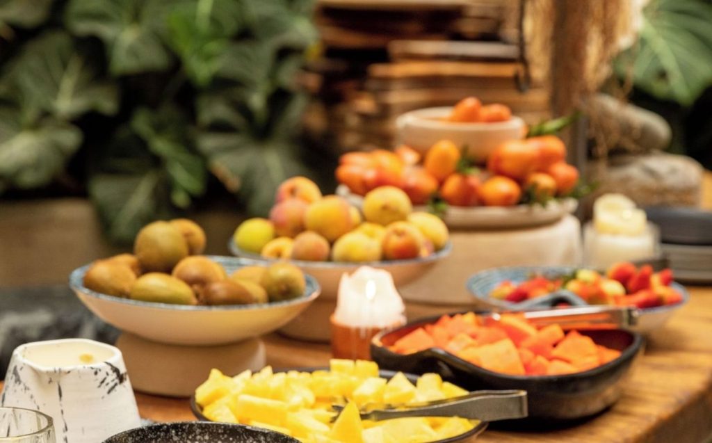 Mesa de buffet con una colorida selección de frutas y verduras frescas en un ambiente de hotel boutique sostenible.