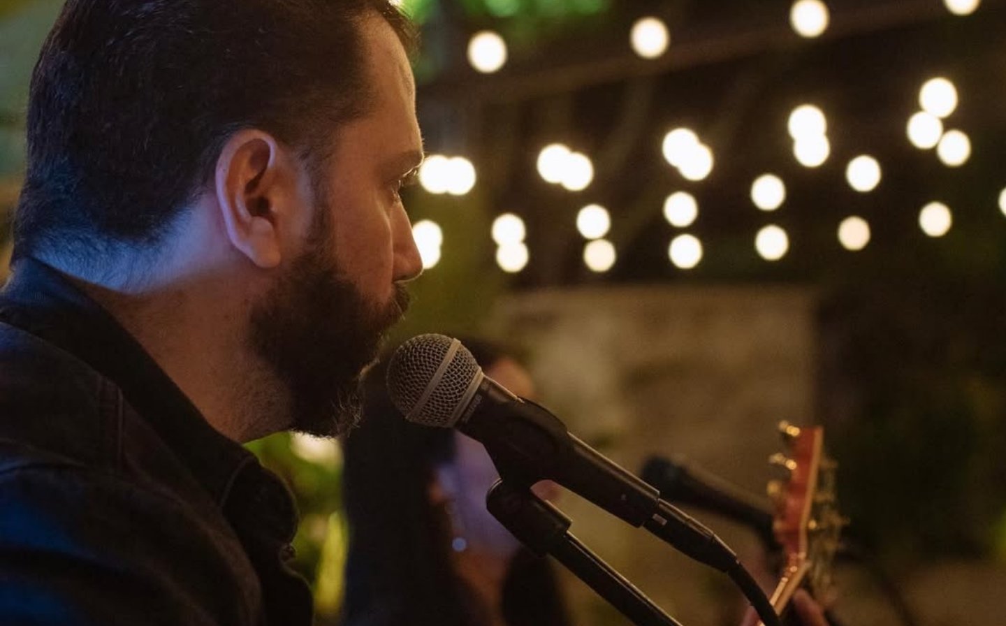 Hombre con barba cantando en un micrófono, creando la banda sonora de una noche perfecta de música en vivo