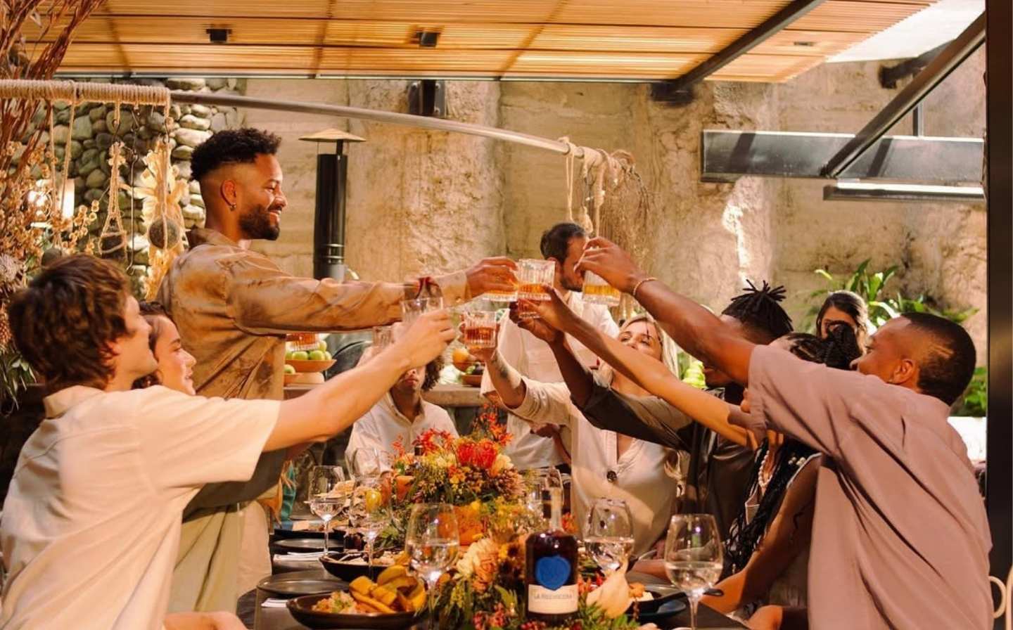 A group of friends joyfully toasting with glasses at a dinner table, celebrating over pizza at Cala Roca
