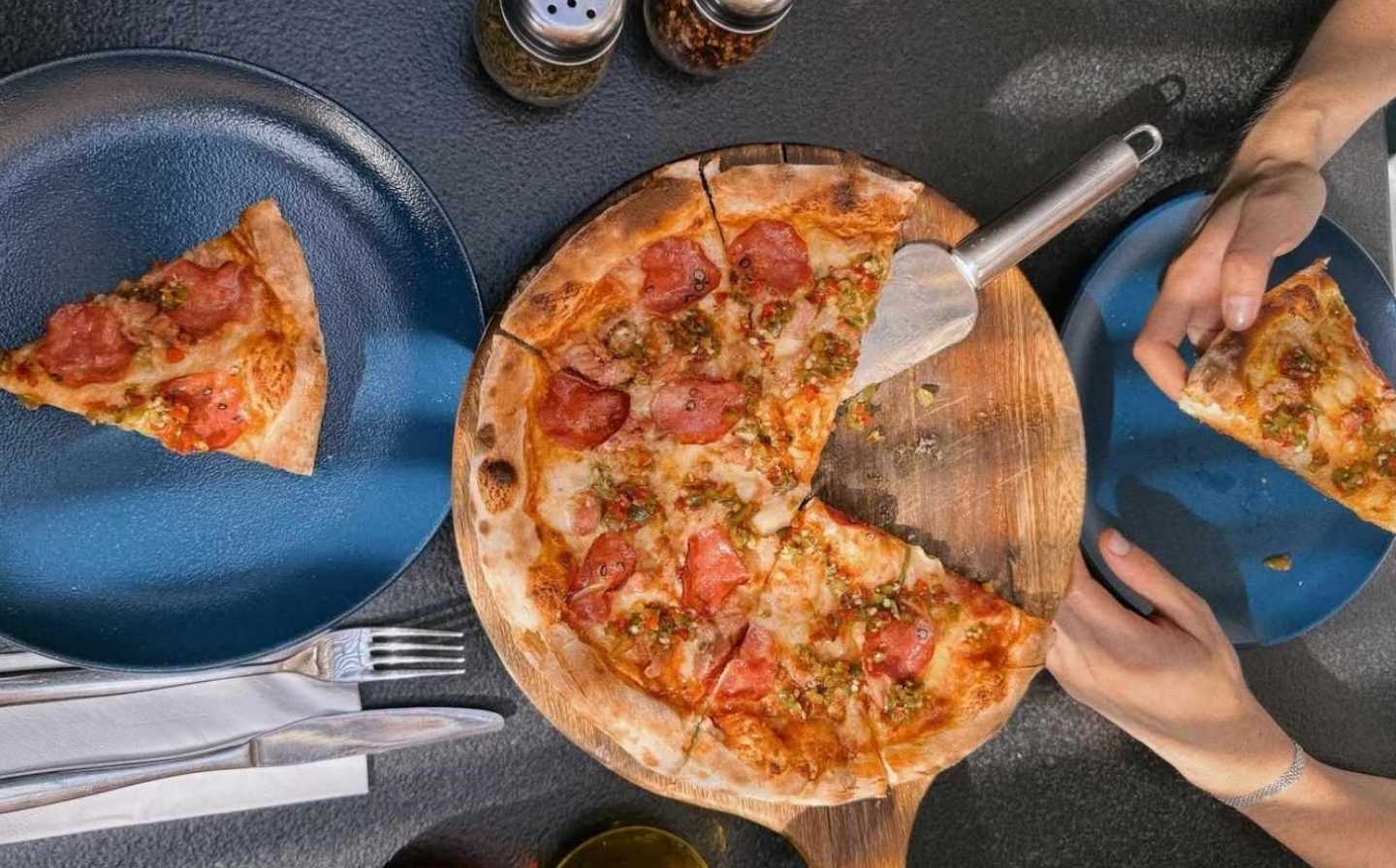 Two people happily cutting a pizza together on a table at Cala Roca, showcasing a fun dining experience