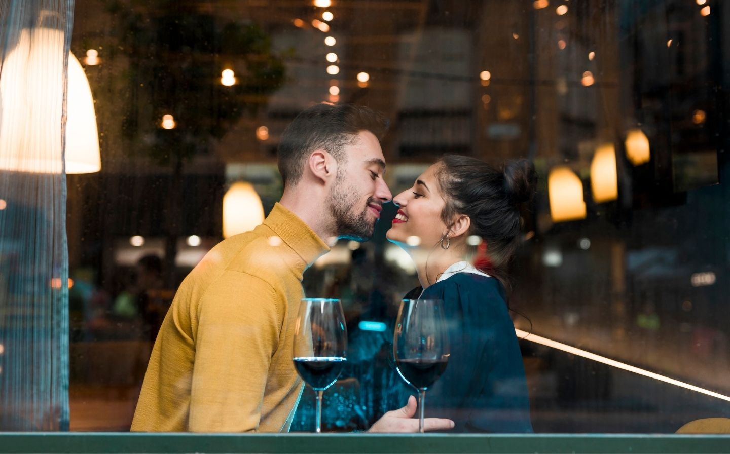 Hombre y mujer besándose frente a una ventana, creando un momento romántico y especial