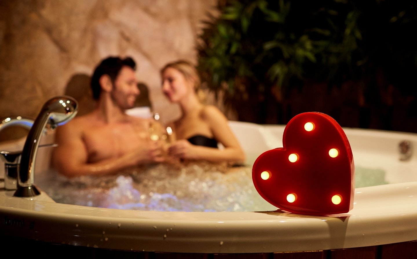 Hombre y mujer disfrutando de un jacuzzi iluminado con una luz en forma de corazón, perfectos para días lluviosos.