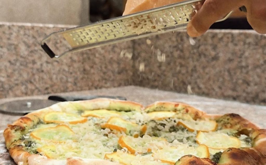 Persona rallando queso sobre una pizza vegana cremosa y mágica