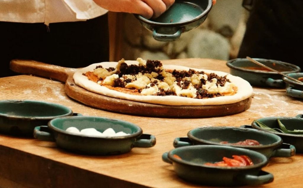 A chef adds colorful toppings to a freshly made pizza on a wooden countertop. Your pizza in 15 minutes.