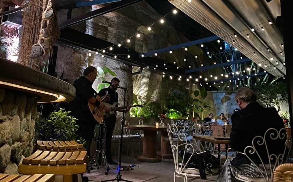 Un hombre toca la guitarra en un restaurante, mientras los comensales disfrutan de su música y compañía