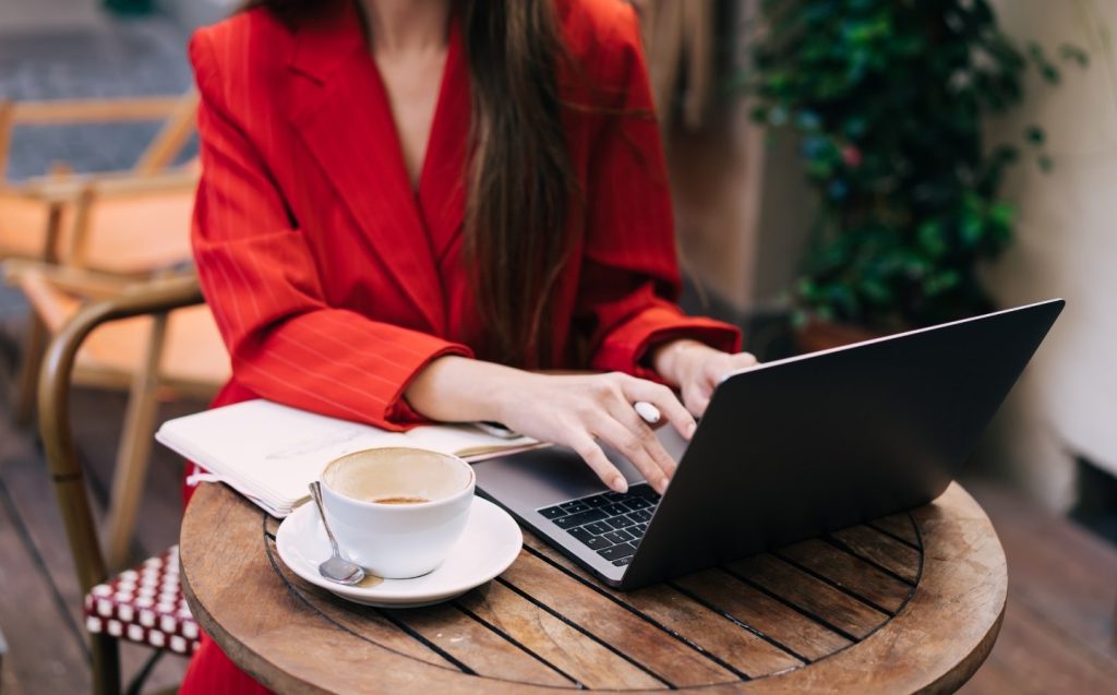 Una mujer con un traje rojo se sienta en una mesa con una computadora portátil en un espacio de coworking.