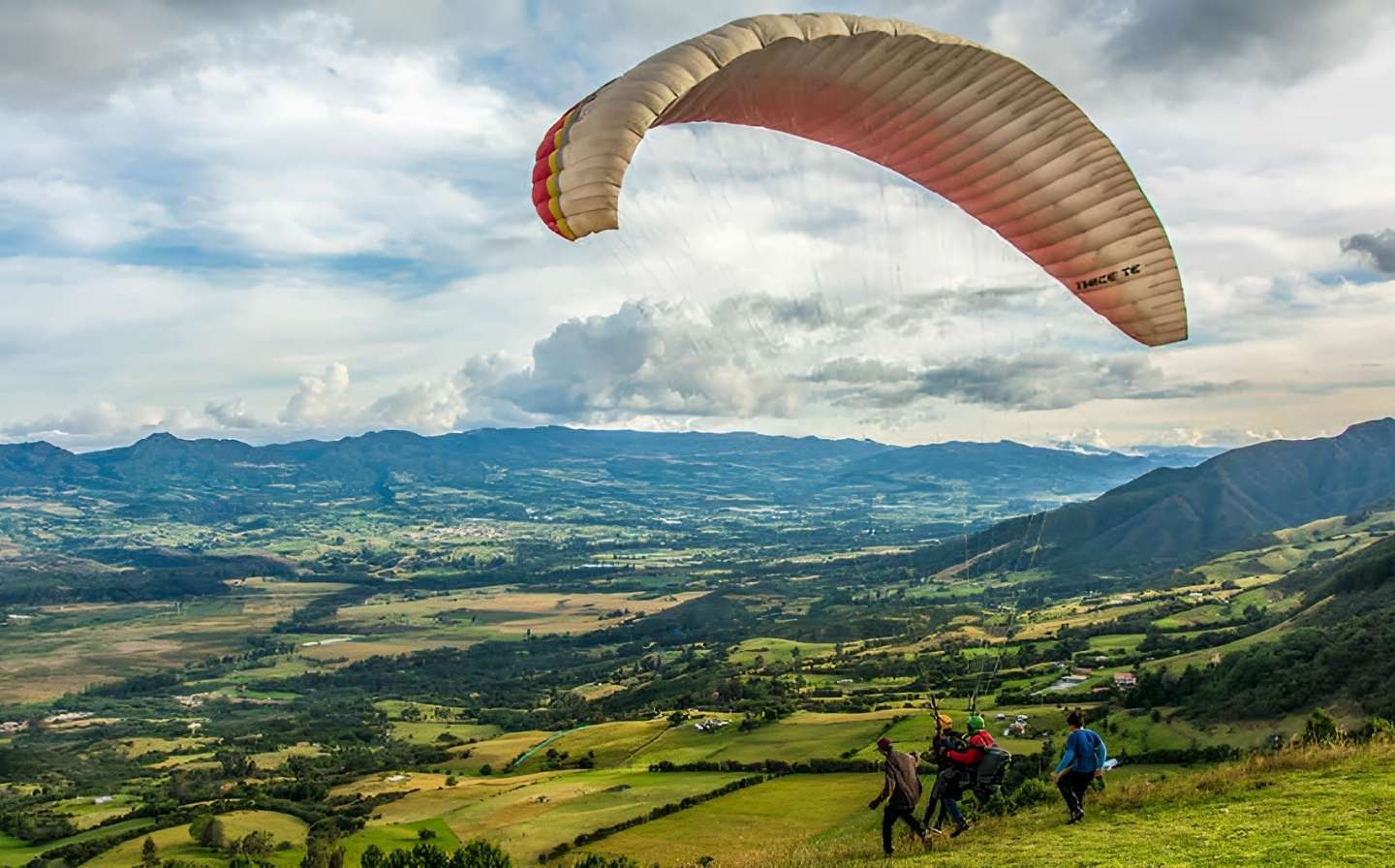 Personas volando en parapente sobre un valle, disfrutando de las memorables vistas en Medellín.