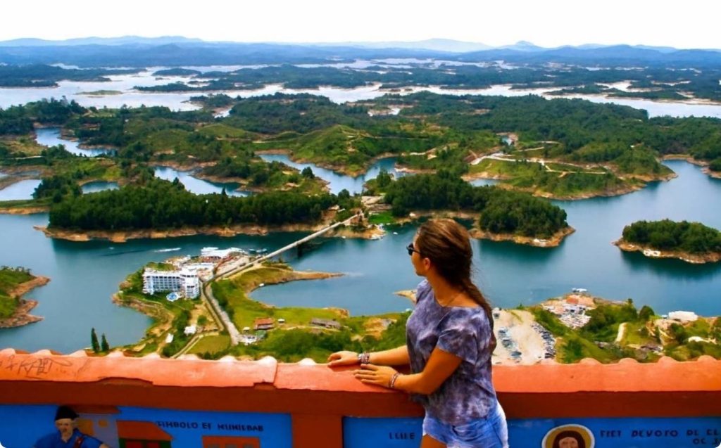 Mujer contemplando un lago y montañas, disfrutando de una excursión de medio día cerca de Medellín.