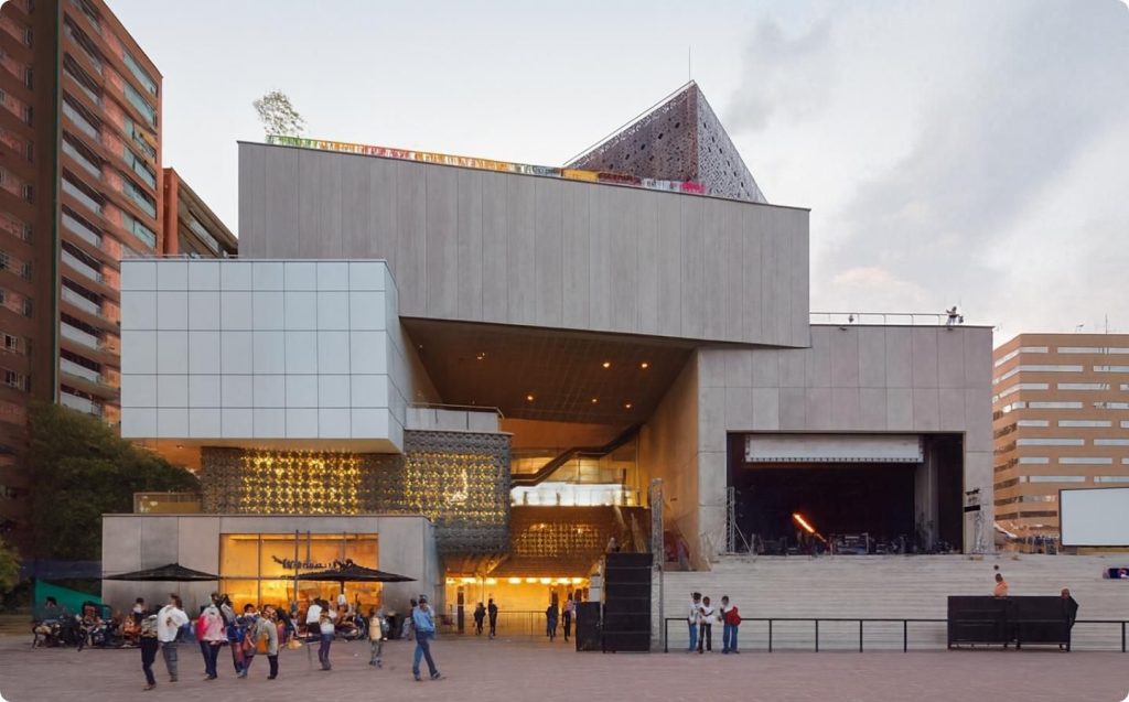 People walking around a large building in Medellín, enjoying the architecture on a rainy day.